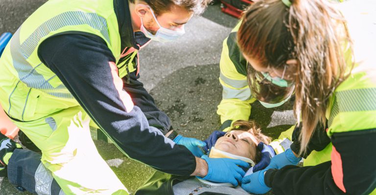 3 paramedics using a collar to immobilize a woman laying down on a road